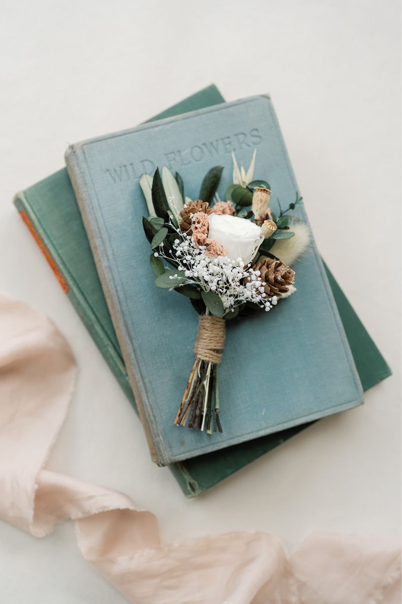 Inspired by crisp winter weddings, this buttonhole is like a mini bouquet filled with a preserved white peony rose, frosted pine cones, oats and foliage, wrapped with twine.