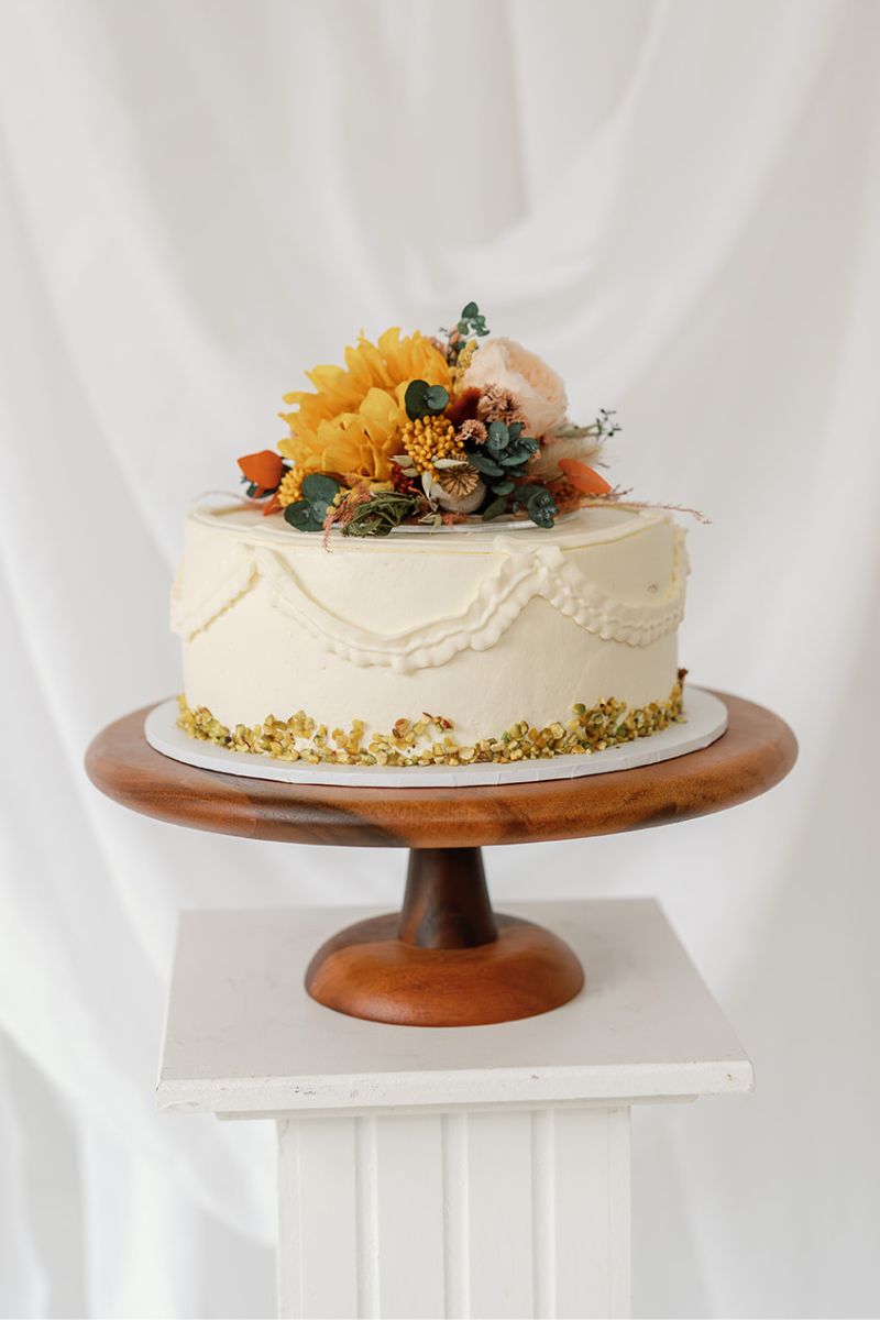 Dried and preserved flower cake topper including yellow preserved sunflowers, peach and nude roses, lush eucalyptus and ferns with pops of terracotta set on a circular acrylic base for food safety.