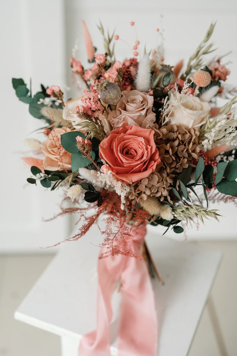 Wildflower style dried flower bridal bouquet featuring coral pink, white and nude flowers with lush greenery and fluffy ferns