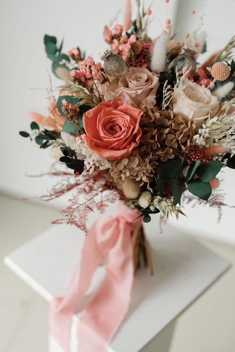 Wildflower style dried flower bridal bouquet featuring coral pink, white and nude flowers with lush greenery and fluffy ferns