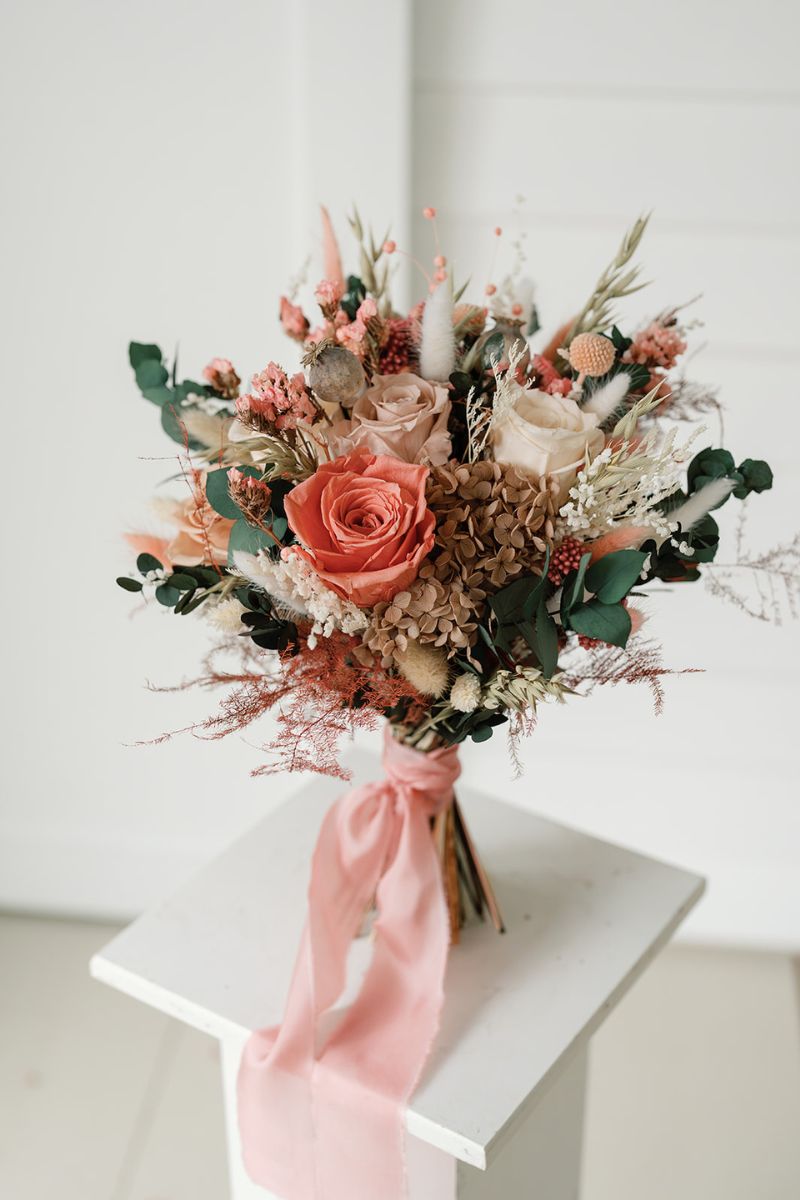 Wildflower style dried flower bridal bouquet featuring coral pink, white and nude flowers with lush greenery and fluffy ferns