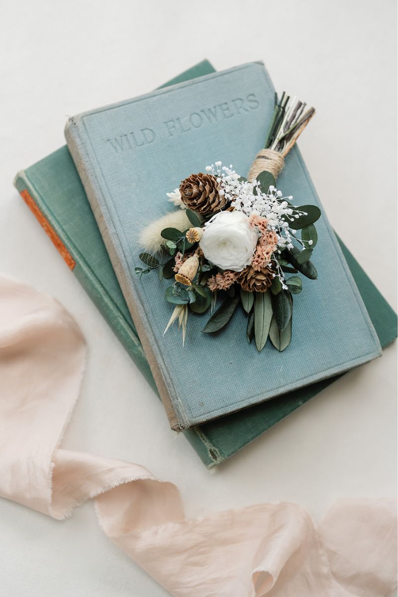 Inspired by crisp winter weddings, this buttonhole is like a mini bouquet filled with a preserved white peony rose, frosted pine cones, oats and foliage, wrapped with twine.