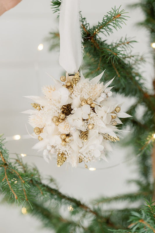Decorative white and gold dried flower ornament on a Christmas tree with lights.