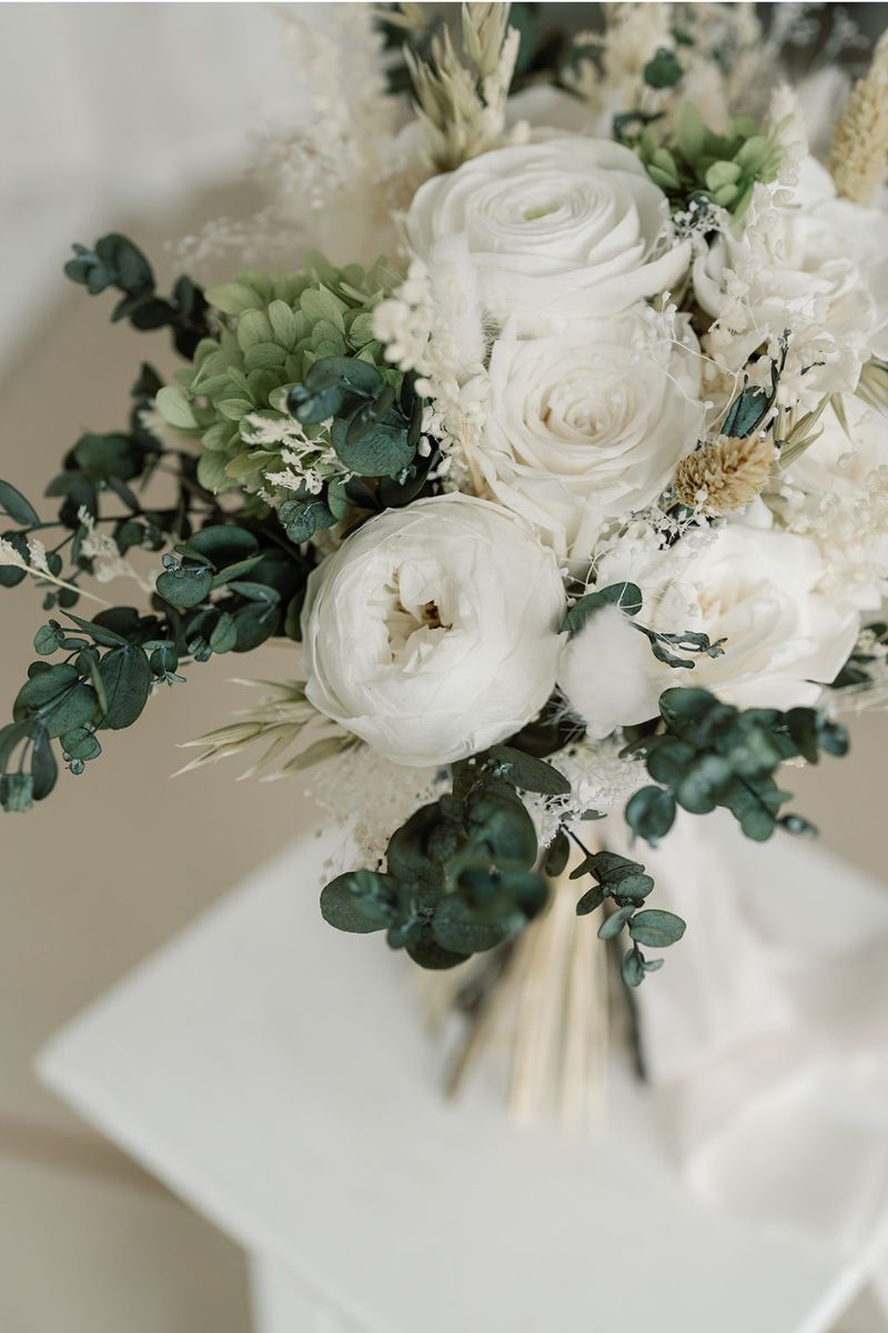 Preserved flower bridal bouquet with white peonies, roses and lime green hydrangea with lush eucalyptus foliage and finished with a silk ribbon around the stems