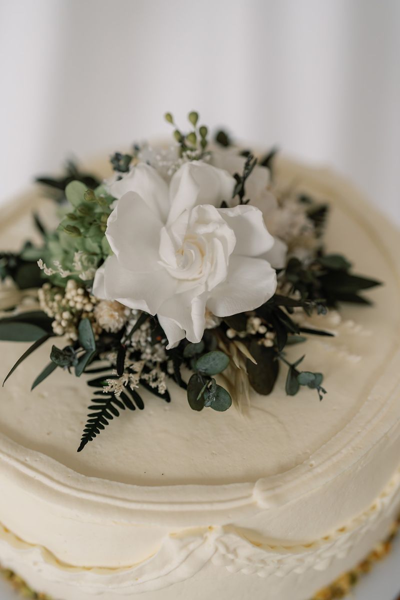 Dried and preserved flower wedding cake topper in white and green colour scheme, the flowers are set on a clear acrylic circular base for food safety.