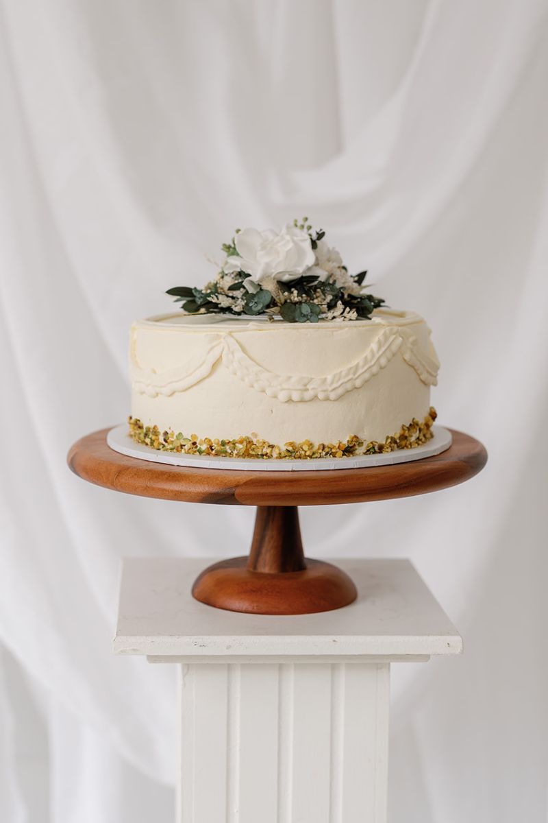 Dried and preserved flower wedding cake topper in white and green colour scheme, the flowers are set on a clear acrylic circular base for food safety.