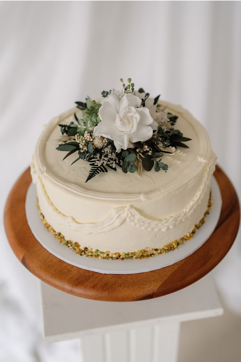Dried and preserved flower wedding cake topper in white and green colour scheme, the flowers are set on a clear acrylic circular base for food safety.
