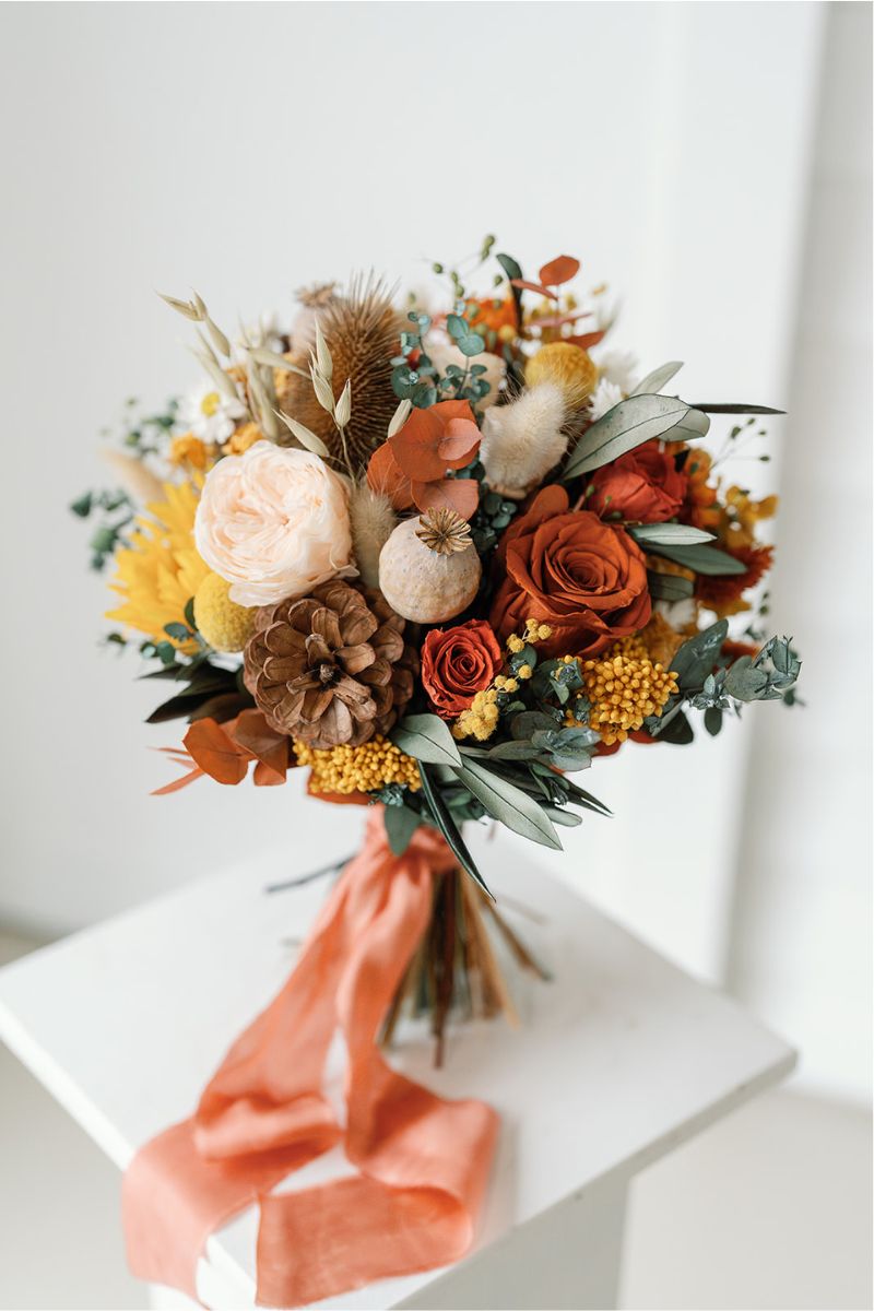 autumnal themed dried flower bridal bouquet in shades of mustard yellow, rust, crowns and lush greenery, hand tied with a rust silk ribbon.