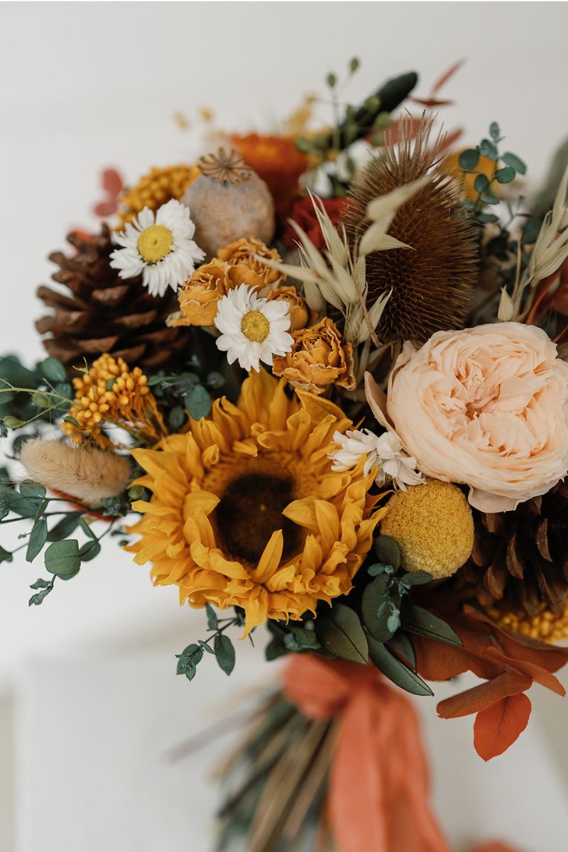 autumnal themed dried flower bridal bouquet in shades of mustard yellow, rust, crowns and lush greenery, hand tied with a rust silk ribbon.