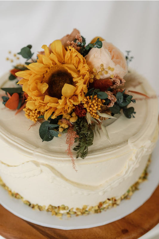 Dried and preserved flower cake topper including yellow preserved sunflowers, peach and nude roses, lush eucalyptus and ferns with pops of terracotta set on a circular acrylic base for food safety.