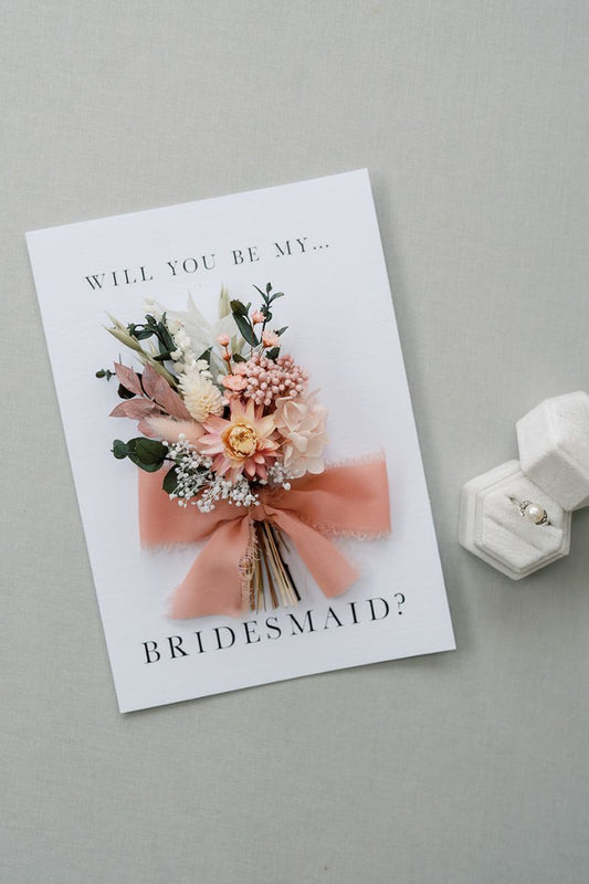 Mini dried flower gift bunch in pale pinks tied onto a bridesmaid proposal card.