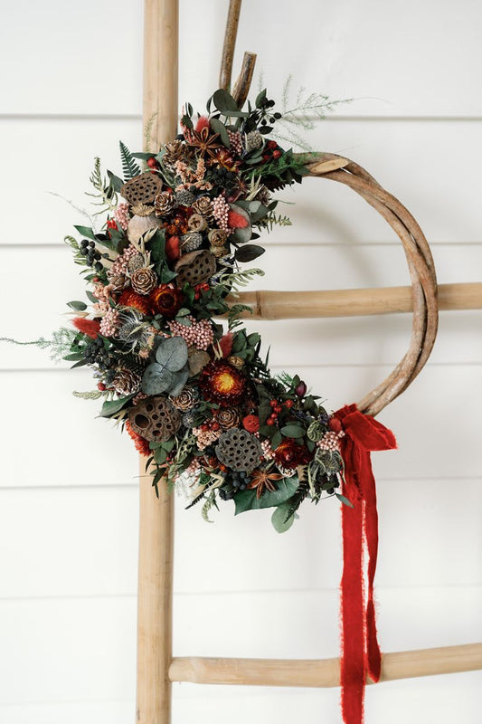 Decorative dried flower Christmas wreath with greenery and red ribbon.